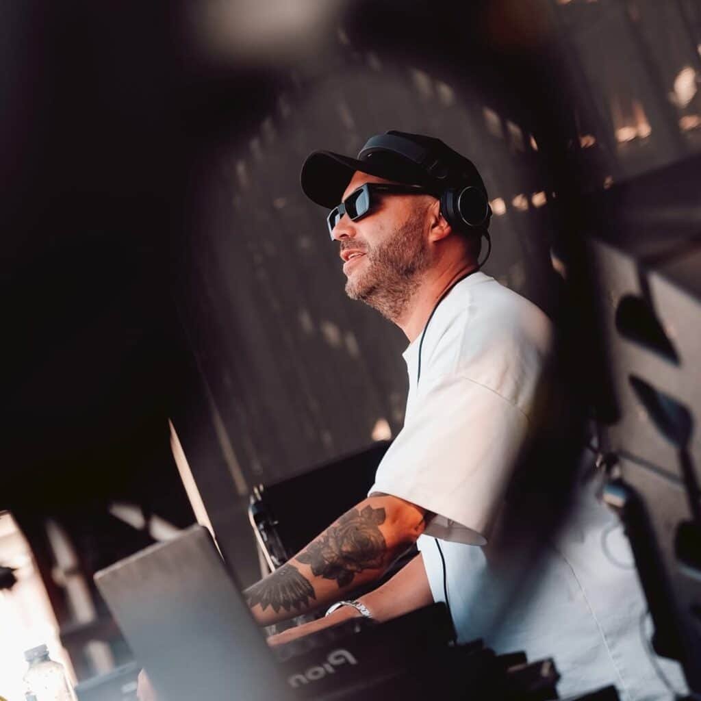 Nic Fanciulli with headphones and sunglasses performs outdoors, surrounded by equipment.