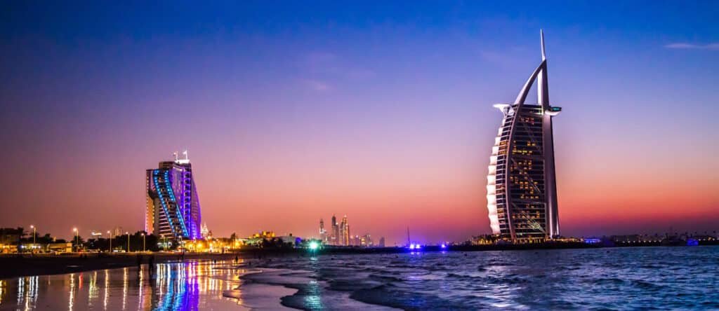Burj Al Arab and Jumeirah Beach Hotel lit up at dusk with a view of the city skyline in the background.