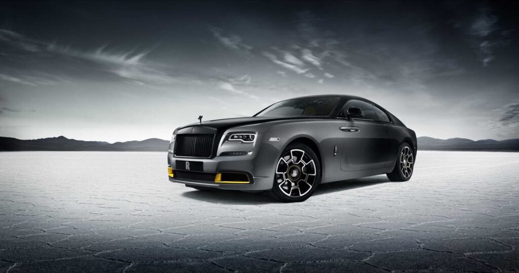 A sleek, dark gray luxury car with distinctive design and intricate wheels, set against a vast, barren landscape.