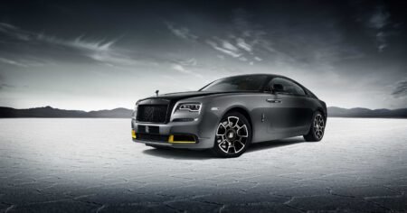 A sleek, dark gray luxury car with distinctive design and intricate wheels, set against a vast, barren landscape.