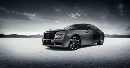 A sleek, dark gray luxury car with distinctive design and intricate wheels, set against a vast, barren landscape.