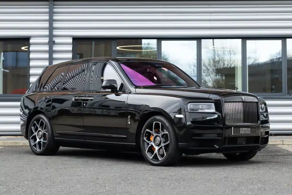 A black luxury SUV with distinctive silver wheels and purple-tinted windows, parked in front of a modern building.