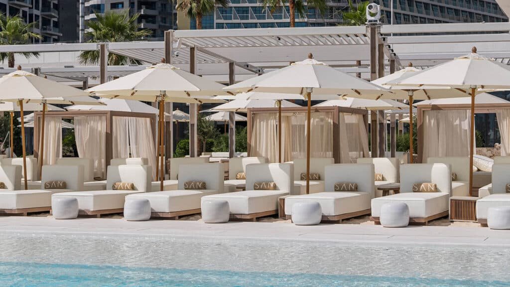 Palm Jumeirah Night Swim: Lounge chairs and white umbrellas line a poolside area with a modern outdoor setting.
