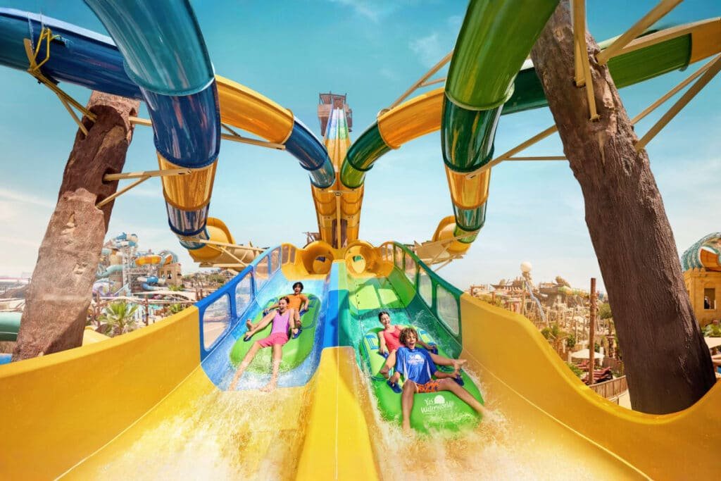 Four people sliding down colorful water slides under a clear blue sky in Yas Waterworld Abu Dhabi.