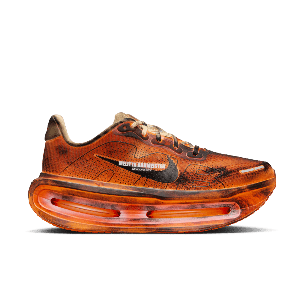 An orange Nike Vomero Premium sneaker with visible air cushioning in the sole and "Reality Randomester" text on the side.