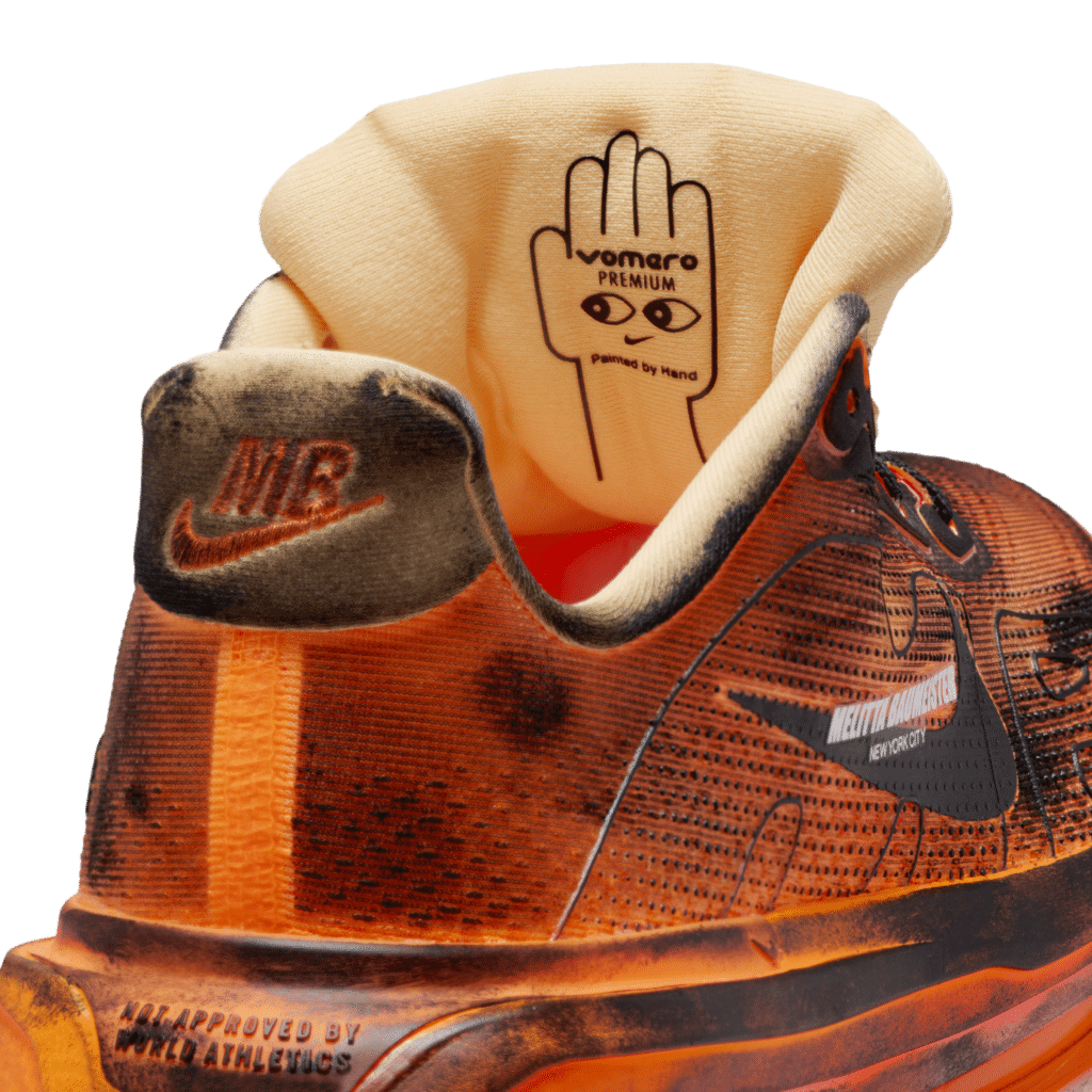 A Vomero Premium sneaker with a burnt orange and black gradient, featuring visible text and a distinctive hand illustration on the tongue.