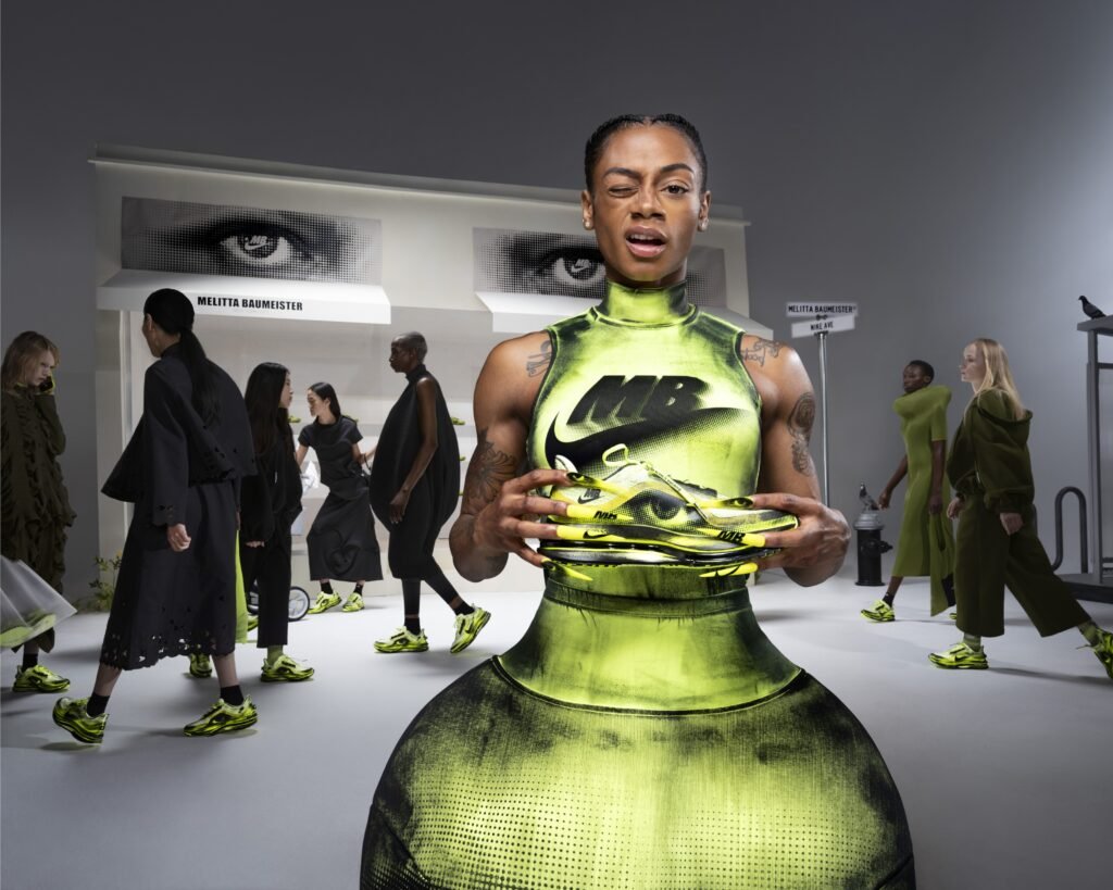 A model in a futuristic dress holds neon green sneakers on a fashion runway with other models wearing matching shoes.