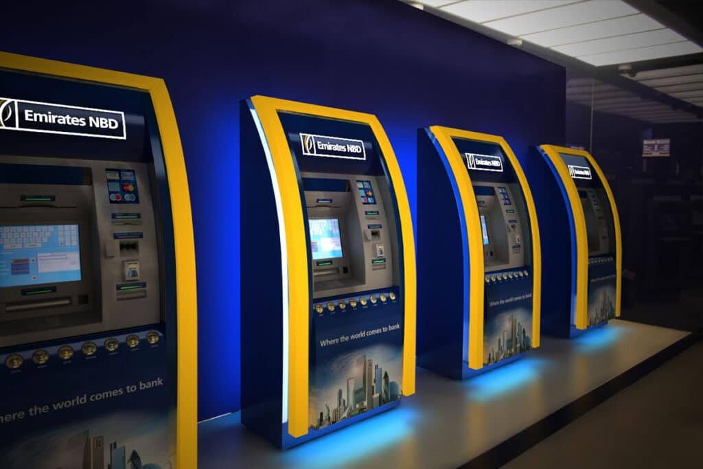 UAE Tourists Can Now Open Digital Bank Accounts on Arrival : A row of Emirates NBD ATMs with blue and yellow exteriors against a dark blue backdrop.