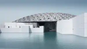 A modern building with a large, intricate dome stands surrounded by water, featuring a pattern that resembles interlocking stars.