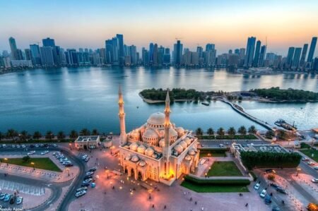 Lit mosque by the waterfront with a city skyline across the bay at sunset
