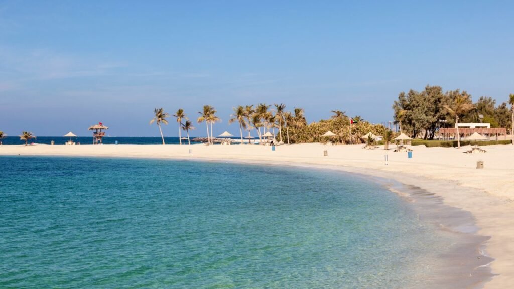 A tranquil beach with palm trees, white sand, and clear blue water under a clear sky.