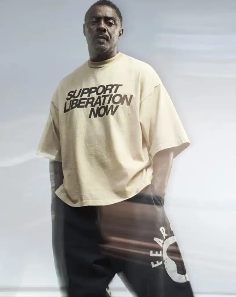Idris Elba wearing a beige Fear of God x Idris Elba Tee