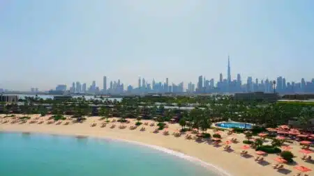 A beach with umbrellas and loungers in the foreground, city skyline with skyscrapers in the background under a clear sky.