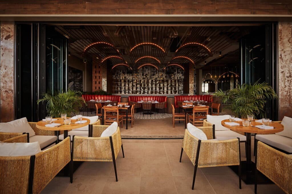 Stylish restaurant interior with woven chairs, round tables set for dining, red banquettes, and arched ceiling lights