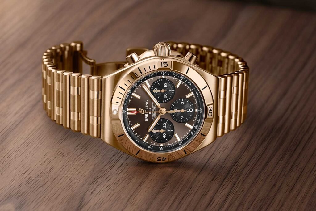 Gold Breitling Chronomat 2026 wristwatch with a black chronograph dial and matching metal bracelet on a wooden surface