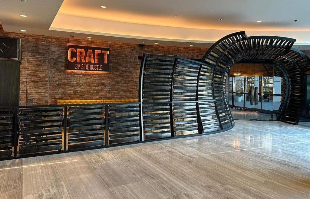 Modern restaurant entrance with a sign reading "Craft by Smoke & Hustle," featuring wood and metal accents on a brick wall.