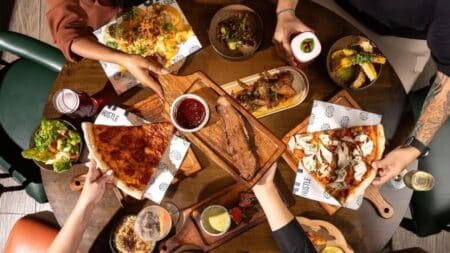 People seated around a table with various dishes, including pizza slices, salads, and sides, sharing a meal together.