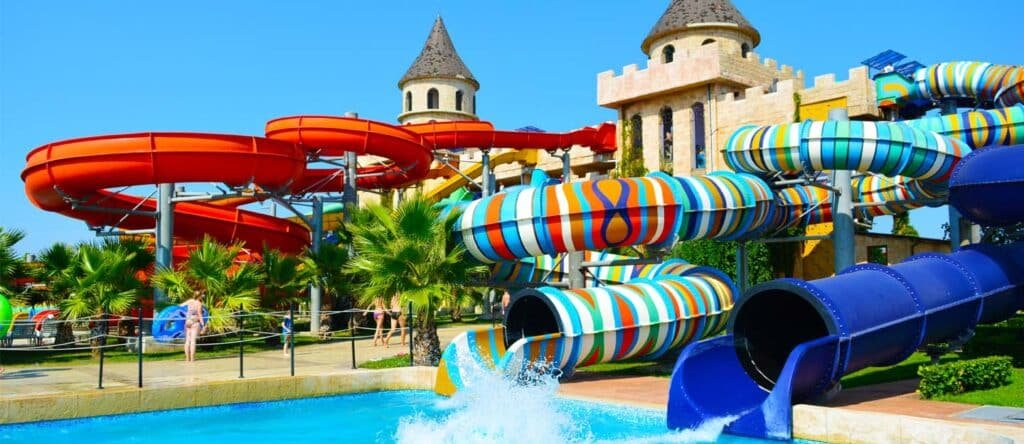 Colorful water slides at a sunny water park with castle-like towers and splashing pools