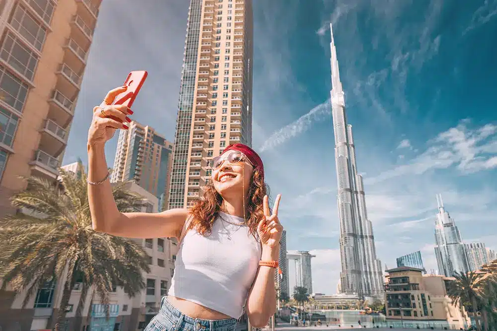 Instagram Purge Hits Dubai: Thousands Lose Followers Overnight A woman takes a selfie near tall skyscrapers, including the Burj Khalifa, on a sunny day.