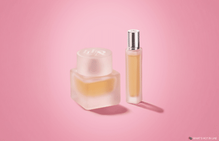 Two frosted perfume bottles with gold liquid on a pink background