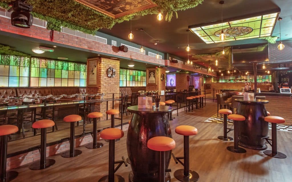 Stylish bar interior with orange stools, high tables, brick walls, and stained-glass ceiling lights