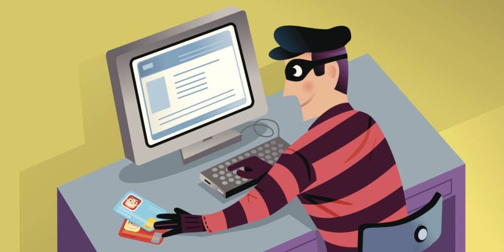Cartoon of a burglar with a mask at a computer, holding ID cards, suggesting Eid Al Adha Scam Alert identity theft.