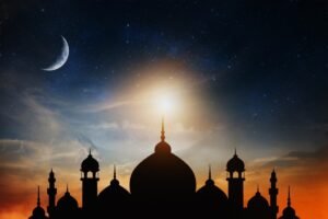Silhouette of a mosque under a starry sky with a crescent moon and a glowing sunset.