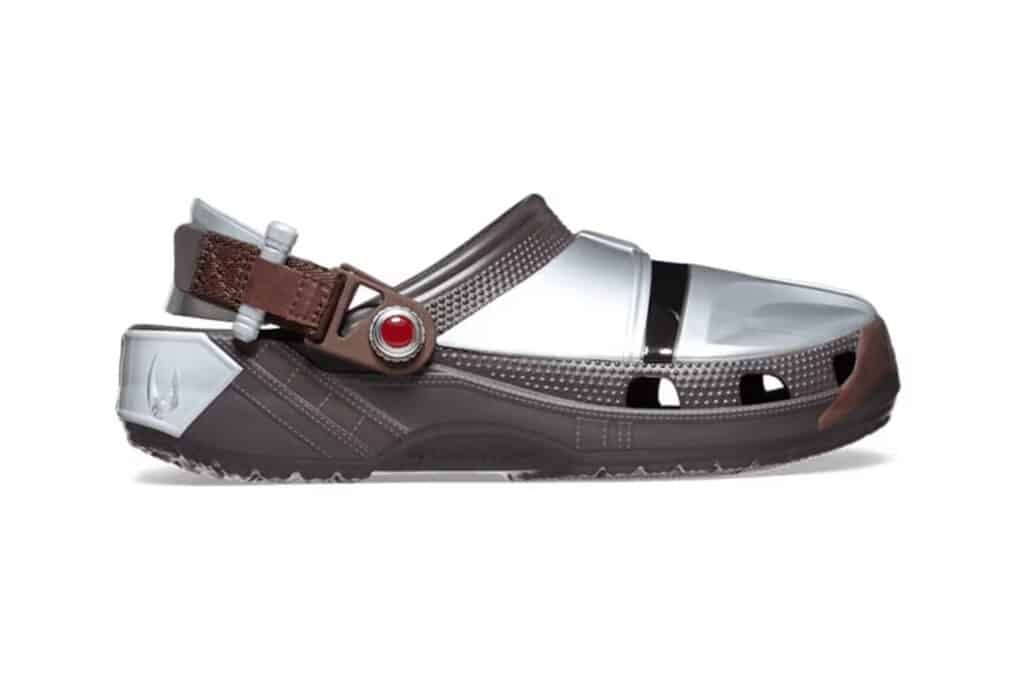 A brown and silver sandal with a futuristic design, featuring an adjustable strap and a red button detail.