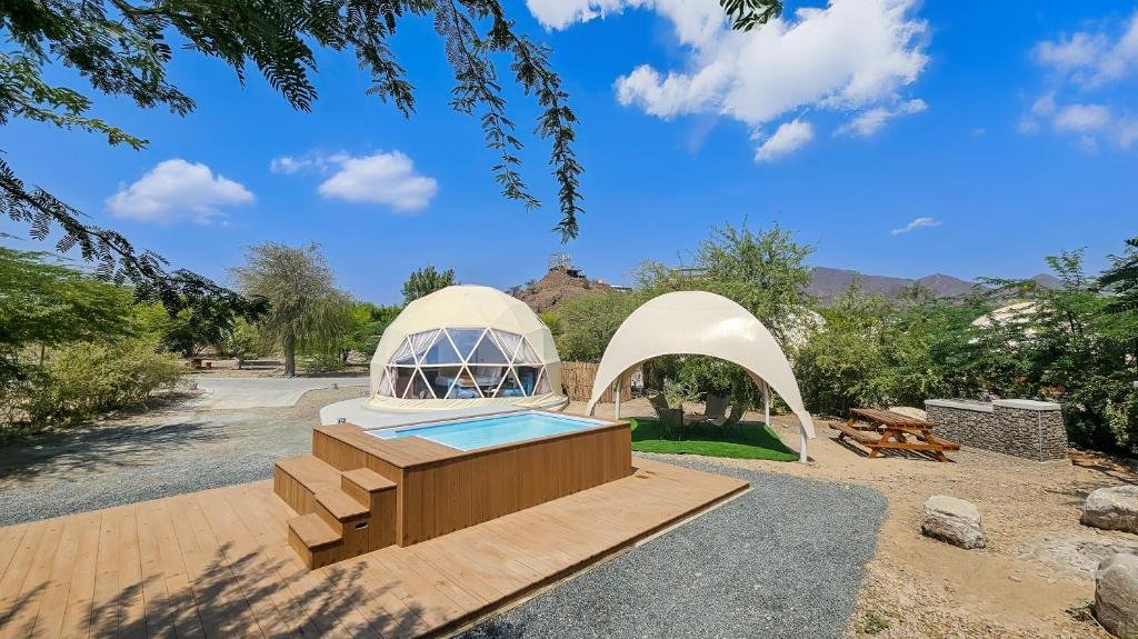 Workcations In The UAE: A glamping site with a dome tent, a small pool on a wooden deck, and an outdoor seating area under a canopy, set in a desert landscape.