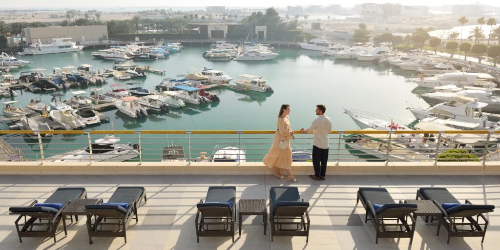 Couple standing by Luxury Staycations In Abu Dhabi a marina railing overlooking many docked yachts and lounge chairs in the foreground