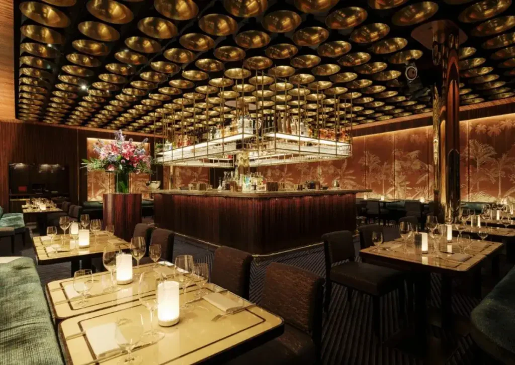 Elegant Isabel Mayfair Abu Dhabi restaurant interior with a luxurious gold ceiling, ambient lighting, floral arrangement, and neatly set tables.