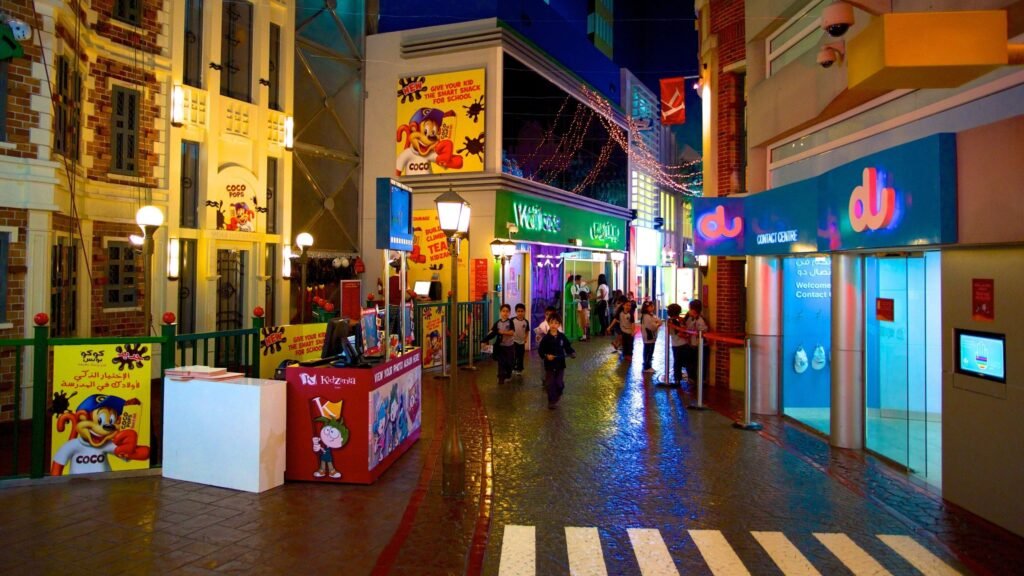 Colorful indoor street scene with children walking past Kidzania storefronts and bright shop signs at night