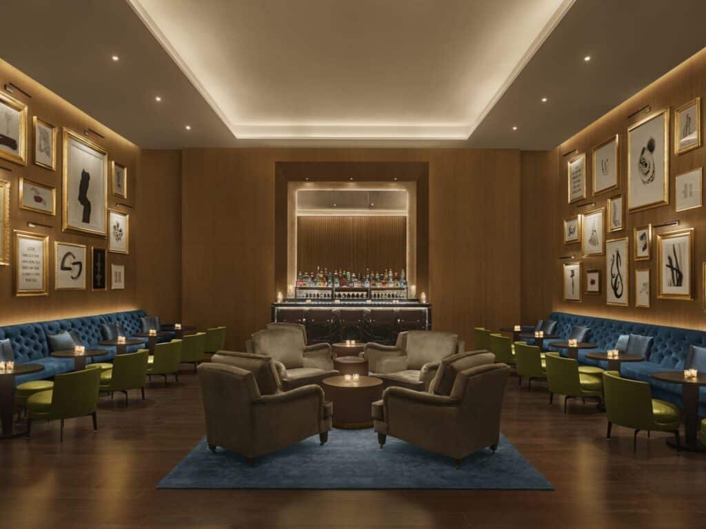 A luxurious lounge with plush armchairs, soft lighting, and artwork on the walls surrounding a central bar.