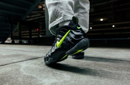 A person wearing black sneakers with neon green accents and a prominent swoosh design walks on a concrete surface.