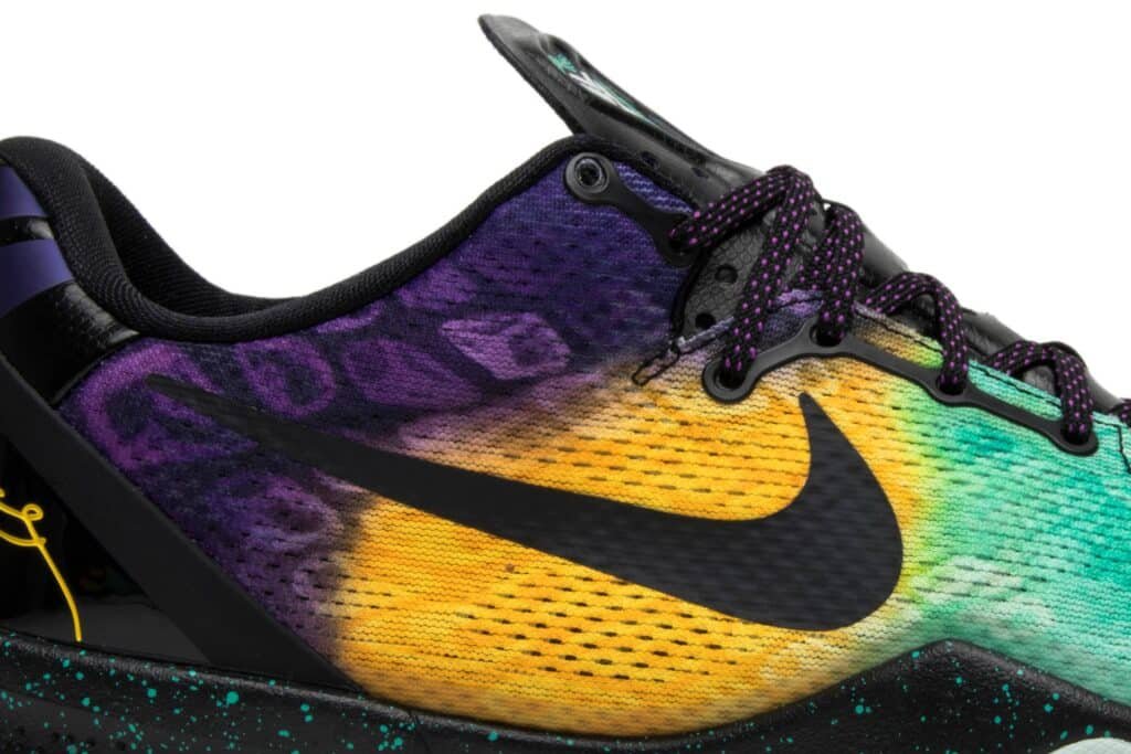 A multicolored shoe featuring a black Nike logo, gradient from purple to yellow to green, and speckled black and teal sole.