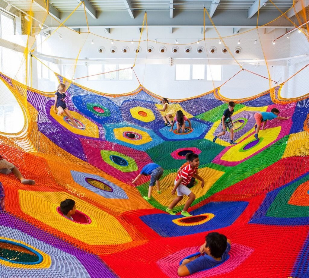 Children playing on a colorful woven net playground suspended indoors