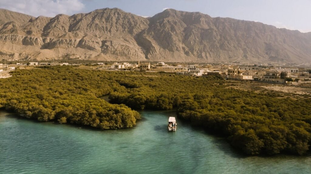 A small boat passes through a turquoise mangrove lagoon with a town and rugged mountains in the background