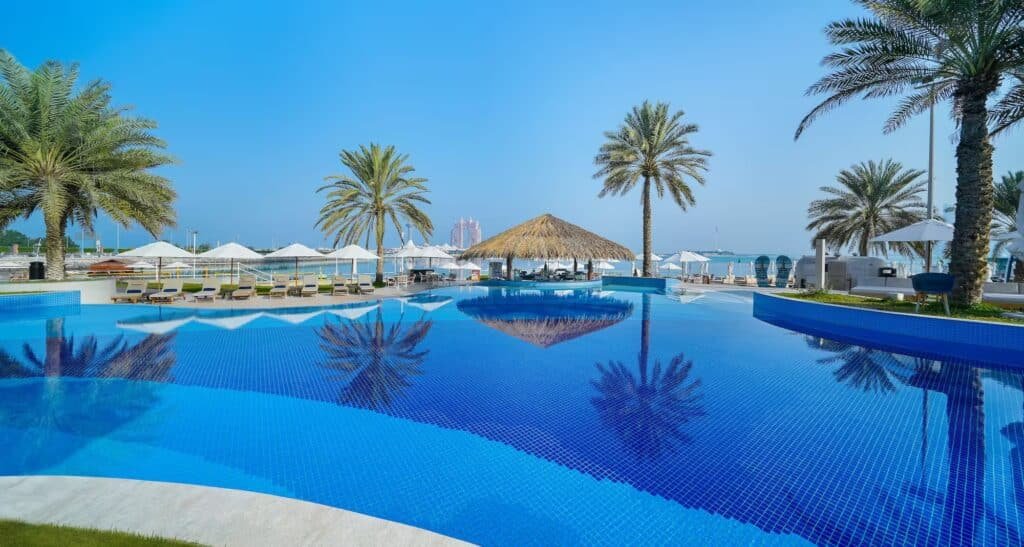 Luxury resort pool with palm trees, lounge chairs, and ocean view under a clear blue sky