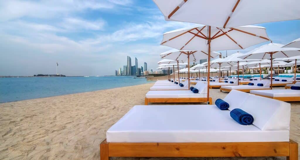Beach resort loungers under white umbrellas with city skyline across the water