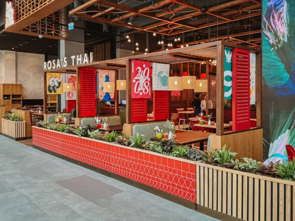 A vibrant Rosa's Thai restaurant with red paneling and colorful decor, featuring potted plants and neatly set tables.