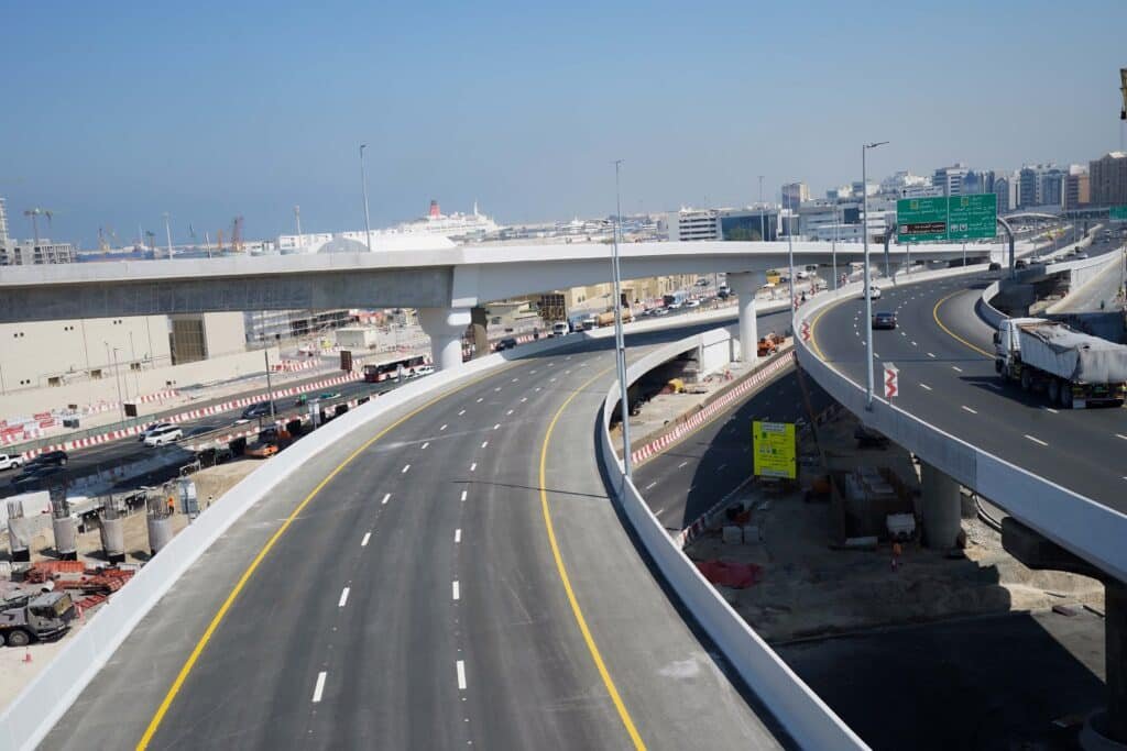 An elevated Sharjah 3-lane Bridge highway interchange in a cityscape, with multiple lanes and overpasses, under a clear blue sky.