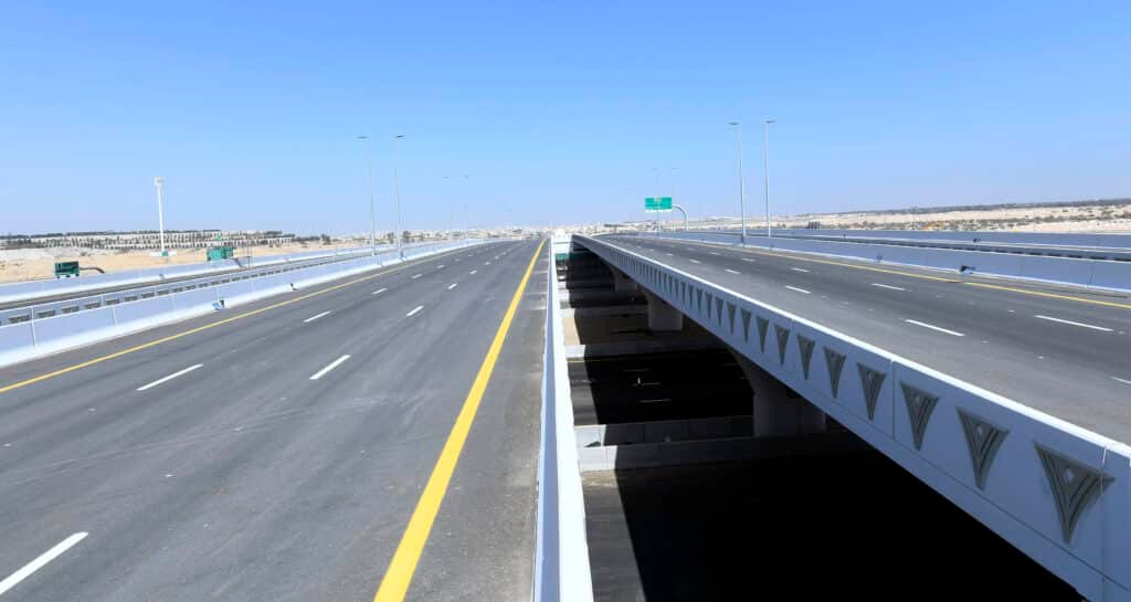 A wide, empty highway with two parallel bridges under a clear blue sky.
