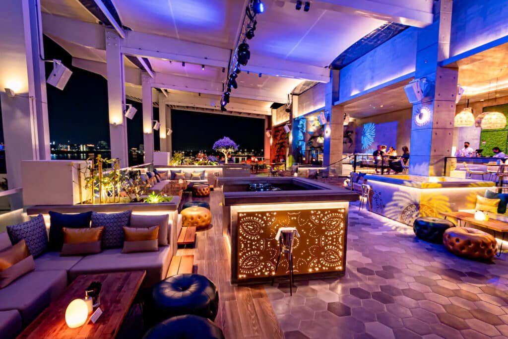 Stylish rooftop bar with ambient lighting, modern decor, and people enjoying the vibrant atmosphere at night.