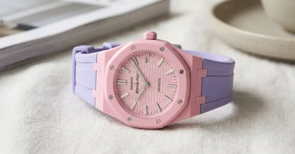 A pink and purple luxury Swatch Audemars Piguet Royal Oak watch with a textured dial, placed on a light fabric surface.