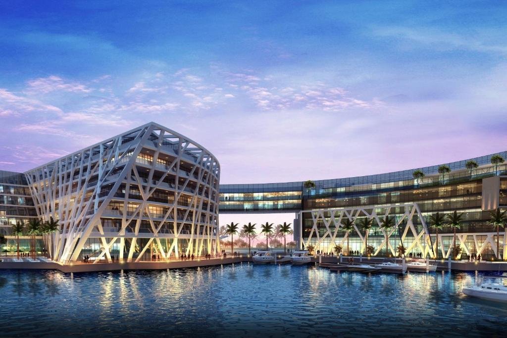 Luxury Staycations In Abu Dhabi: Modern waterfront complex with illuminated glass buildings and a marina at sunset