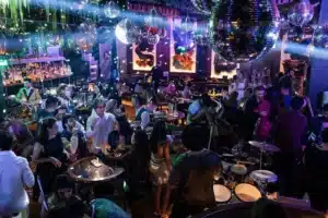 A crowded nightclub with people dancing and socializing under large disco balls and colorful lights.