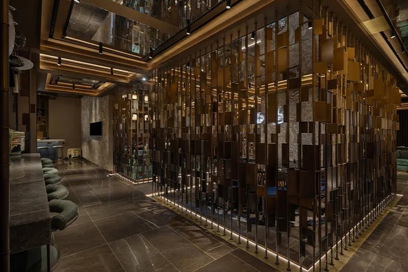 A dimly lit modern lounge with a mirrored geometric partition, bar seating, and dark tiled floors