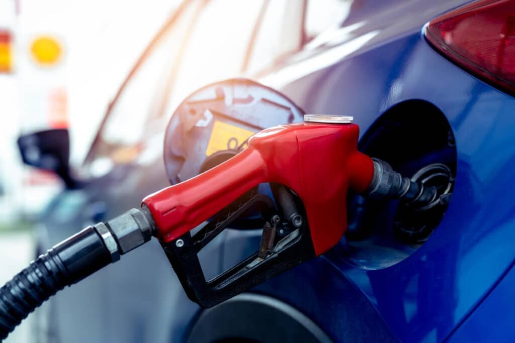 A red gas pump nozzle inserted into a blue car at a fuel station.