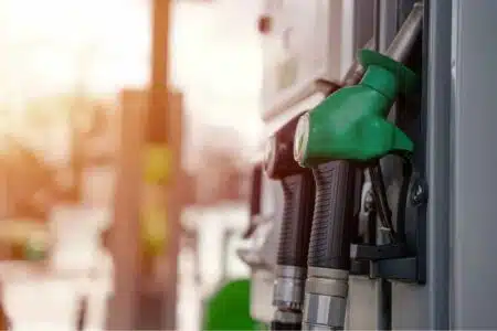 Green fuel pump nozzle at a gas station with a blurred background.
