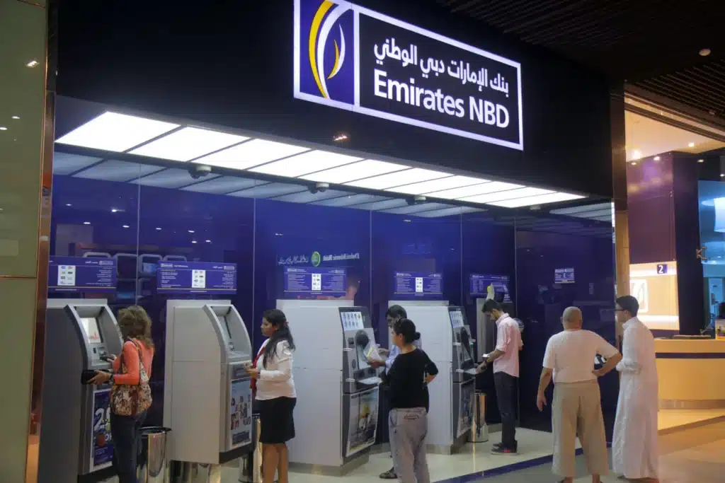 People using ATMs at an Emirates NBD branch, with a blue and white sign overhead.